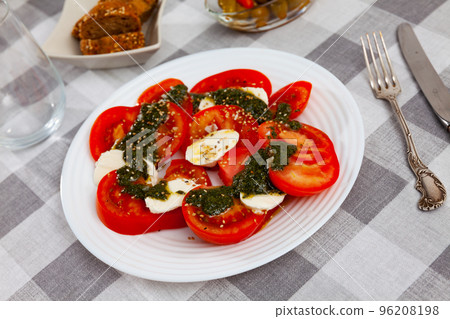 Caprese salad with fresh tomatoes and mozzarella seasoned with pesto 96208198
