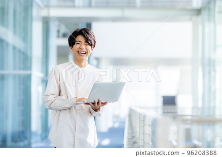 Young man standing with laptop in office lobby Young man standing with laptop in office lobby 96208388