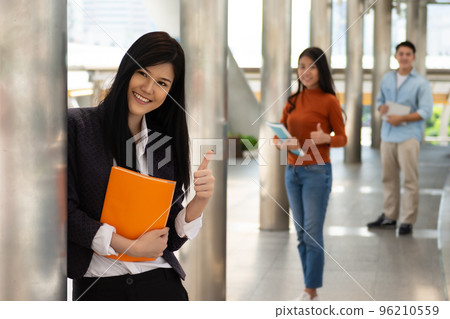 Young Asian woman holding books and smiling raised thumbs up in the university, people education concept.. Young Asian woman holding books and smiling raised thumbs up in the university, people education concept.. 96210559