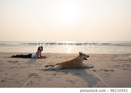 Young healthy woman and dog doing Upward Dog Yoga Position on the beach... Young healthy woman and dog doing Upward Dog Yoga Position on the beach... 96210561