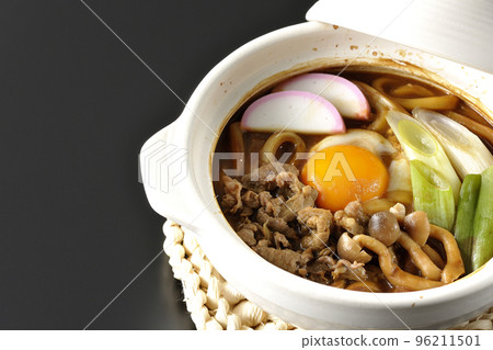 Miso-nikomi udon with beef, shimeji mushrooms, green onion, kamaboko, and egg yolk photographed against a black background 96211501