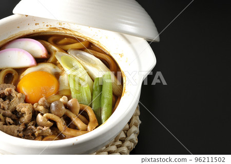 Miso-nikomi udon with beef, shimeji mushrooms, green onion, kamaboko, and egg yolk photographed against a black background 96211502