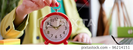Businesswoman holding red alarm clock at workplace Businesswoman holding red alarm clock at workplace 96214151