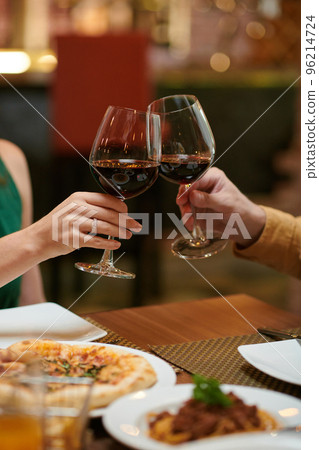 Cropped image of couple toasting with glasses or red wine over dinner table in restaurant 96214724