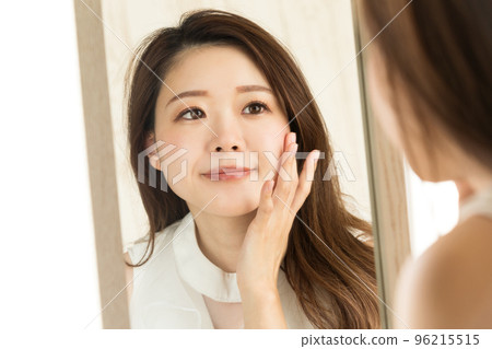 一個女人照鏡子時正在做皮膚護理。 一個女人照鏡子時正在做皮膚護理。 96215515