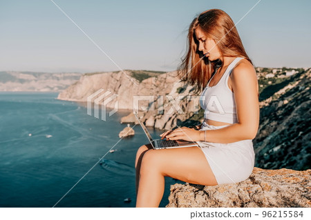 Digital nomad, Business woman working on laptop by the sea. Pretty lady typing on computer by the sea at sunset, makes a business transaction online from a distance. Freelance, remote work on vacation Digital nomad, Business woman working on laptop by the sea. Pretty lady typing on computer by the sea at sunset, makes a business transaction online from a distance. Freelance, remote work on vacation 96215584
