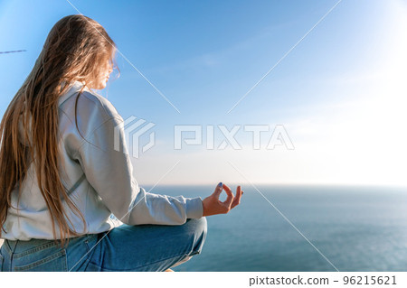 A young tourist Woman enjoying sunset over sea mountain landscape while sitting outdoor. Women's yoga fitness routine. Healthy lifestyle, harmony and meditation 96215621
