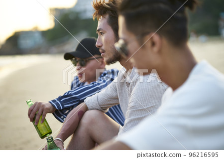 three young asian adult men sitting on beach drinking beer three young asian adult men sitting on beach drinking beer 96216595