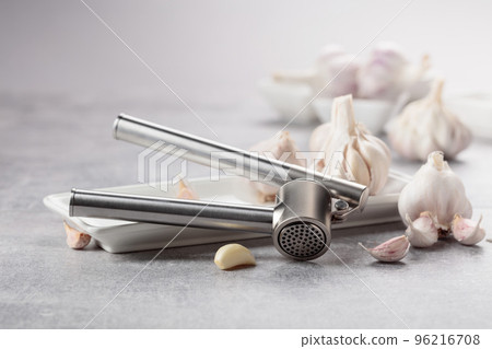 Garlic and garlic press on a grey table. 96216708