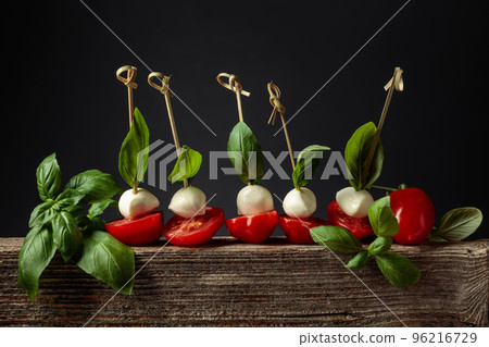 Mozzarella with basil and tomatoes on an old wooden board. 96216729