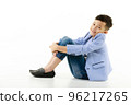 A 10-year-old Asian boy in a casual jacket is sitting on the ground, hands on his knees and smiling cheerfully, looking at the camera. 96217265