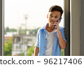 A young boy, an Asian elementary school student, is holding a smartphone calling and talking to someone. 96217406