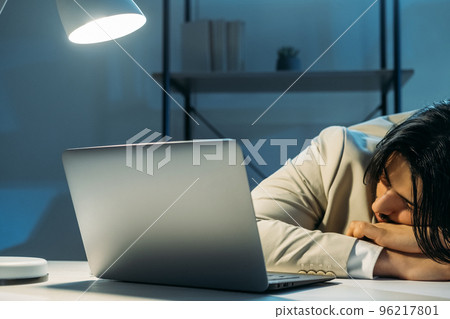 Late work. Tired man. Project deadline. Office guy in elegant suit falling asleep sitting desk opened laptop dark light room interior. Late work. Tired man. Project deadline. Office guy in elegant suit falling asleep sitting desk opened laptop dark light room interior. 96217801