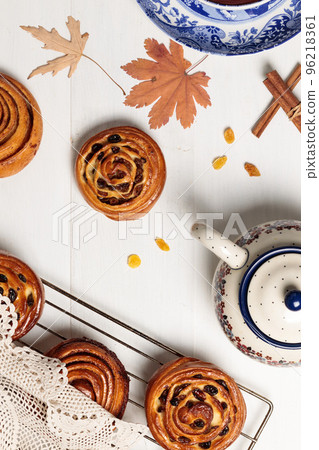 Homemade buns with raisins and cinnamon, a teapot with tea, on a light wooden background. Homemade buns with raisins and cinnamon, a teapot with tea, on a light wooden background. 96218361