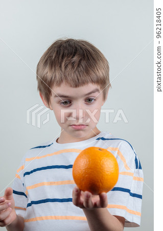 The blond guy looks thoughtfully at the orange in his hands. Portrait, selective focus 96218405