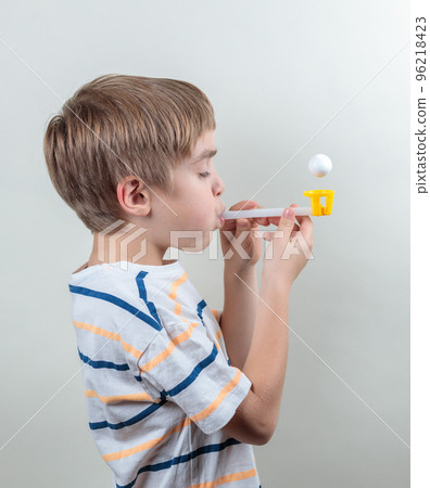 Breathing exercises with a simulator. The boy breathes into a tube, blows out a ball. Complex therapy after pneumonia Breathing exercises with a simulator. The boy breathes into a tube, blows out a ball. Complex therapy after pneumonia 96218423