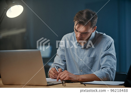 young businessman taking notes in his notebook during night work. young businessman taking notes in his notebook during night work. 96218488
