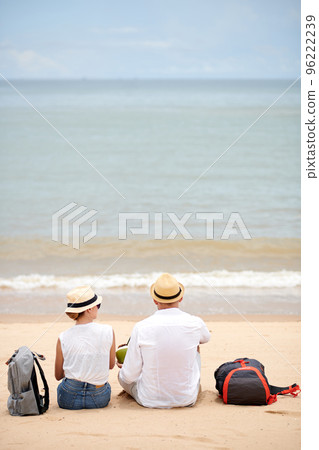Couple with backpacks sitting on beach, drinking coconut cocktails and looking at waves Couple with backpacks sitting on beach, drinking coconut cocktails and looking at waves 96222239