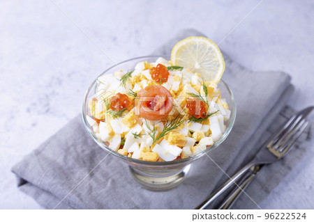 Layered salad with salted trout (salmon), caviar, eggs and vegetables. Traditional dish, one portion in a glass goblet on a gray background. Close-up. Layered salad with salted trout (salmon), caviar, eggs and vegetables. Traditional dish, one portion in a glass goblet on a gray background. Close-up. 96222524