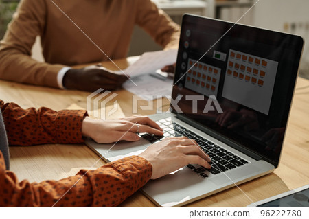 Close-up of businesswoman typing on laptop while sitting at table with colleagues at meeting 96222780