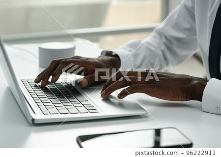 Close-up of African American businessman typing on laptop and doing his online work at table at office Close-up of African American businessman typing on laptop and doing his online work at table at office 96222911