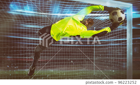 Soccer goalkeeper, in fluorescent uniform, makes a save and avoids a goal during a night match Soccer goalkeeper, in fluorescent uniform, makes a save and avoids a goal during a night match 96223252