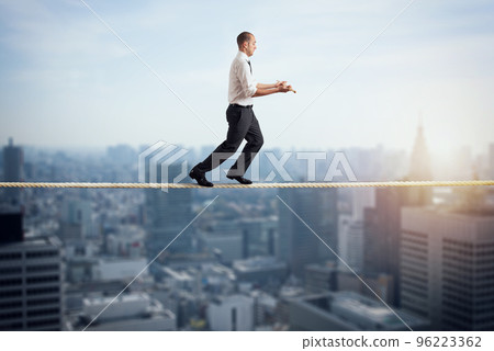 Worry man in balance walking on a rope over a city 96223362