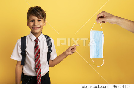Young smiling student indicates a face mask for covid19. yellow background Young smiling student indicates a face mask for covid19. yellow background 96224104