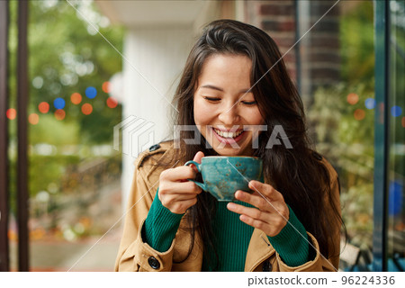 Portrait of cute young Asian woman drinking coffee on terrace of cafe. Outdoors. Cozy autumn season 96224336