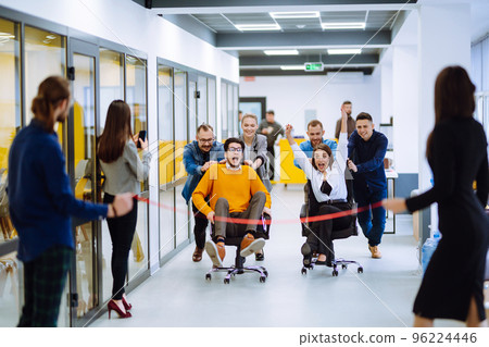 Young colleagues group having fun together, riding on chairs in office 96224446
