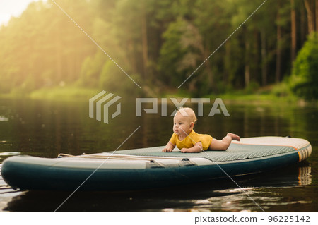The child lies floating on the water on a large sup board. Water sports 96225142