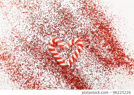 Christmas composition with candy canes in form oh heart on blue wooden background with red sequins Christmas composition with candy canes in form oh heart on blue wooden background with red sequins 96225226