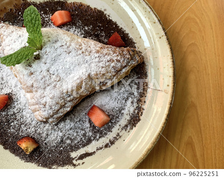 Apple turnovers dusted with icing sugar with strawberry chunks and chocolate sauce 96225251
