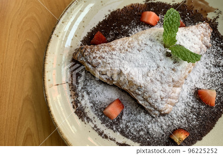 Apple turnovers dusted with icing sugar with strawberry chunks and chocolate sauce 96225252