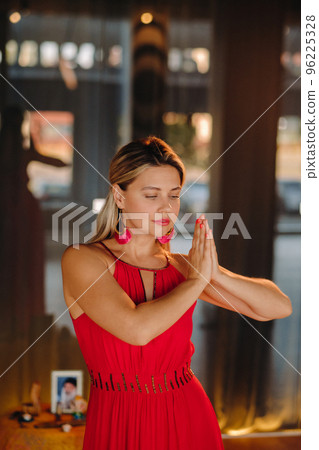 Portrait of a smiling girl in a red dress stands in the interior with her hands clasped in front of her Portrait of a smiling girl in a red dress stands in the interior with her hands clasped in front of her 96225328