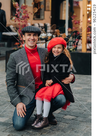 Portrait of a father and daughter sitting on a knee and being on a city street in autumn 96225419