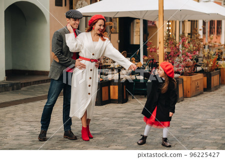 A stylish family of three strolls through the autumn city posing for a photographer . Dad, mom and daughter in the autumn city 96225427