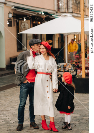 A stylish family of three strolls through the autumn city posing for a photographer . Dad, mom and daughter in the autumn city 96225428