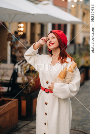Portrait of a pretty woman in a red beret and a white cardigan with baguettes in her hands strolling through the autumn city Portrait of a pretty woman in a red beret and a white cardigan with baguettes in her hands strolling through the autumn city 96225458