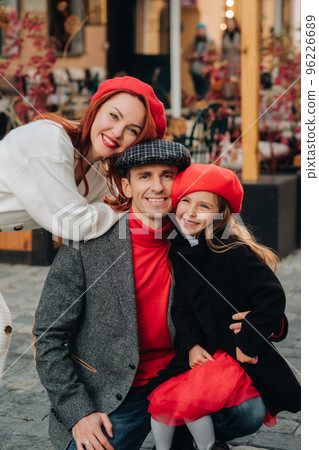 A stylish family of three strolls through the autumn city posing for a photographer . Dad, mom and daughter in the autumn city A stylish family of three strolls through the autumn city posing for a photographer . Dad, mom and daughter in the autumn city 96226689