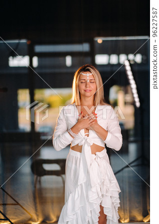 Portrait of a smiling girl in a white dress with her palms clasped in front of her Portrait of a smiling girl in a white dress with her palms clasped in front of her 96227587