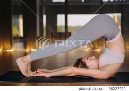 The girl does yoga. A woman in sports clothes does yoga exercises in the gym The girl does yoga. A woman in sports clothes does yoga exercises in the gym 96227931