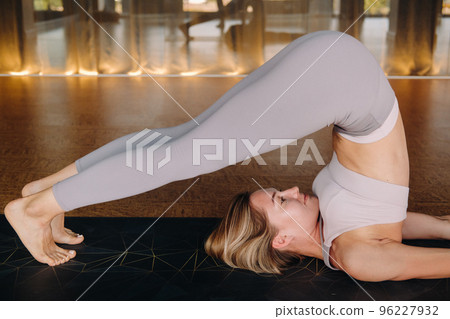 The girl does yoga. A woman in sports clothes does yoga exercises in the gym The girl does yoga. A woman in sports clothes does yoga exercises in the gym 96227932