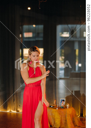 A girl in a red dress moves in a dance meditating indoors . Dynamic dance 96228052