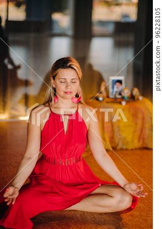 Meditation and concentration. a woman in a red dress, sitting on the floor with her eyes closed, is practicing medicine indoors. Peace and relaxation 96228105