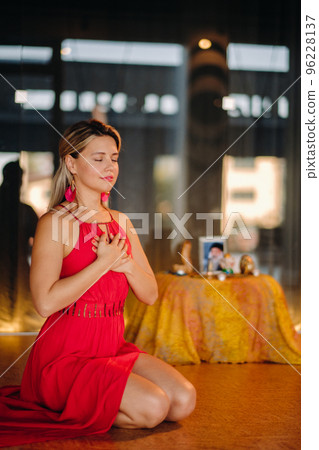 Meditation and concentration. a woman in a red dress, sitting on the floor with her eyes closed, is practicing medicine indoors. Peace and relaxation 96228137