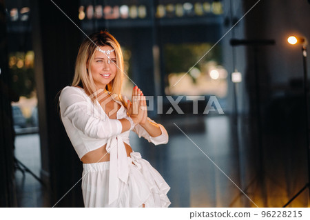Portrait of a smiling girl in a white dress with her palms clasped in front of her 96228215