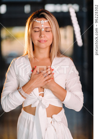 Portrait of a smiling girl in a white dress with her palms clasped in front of her Portrait of a smiling girl in a white dress with her palms clasped in front of her 96228302