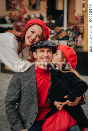 A stylish family of three strolls through the autumn city posing for a photographer . Dad, mom and daughter in the autumn city 96228449