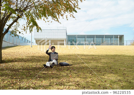 A man sitting on the lawn and using a laptop A man sitting on the lawn and using a laptop 96228535